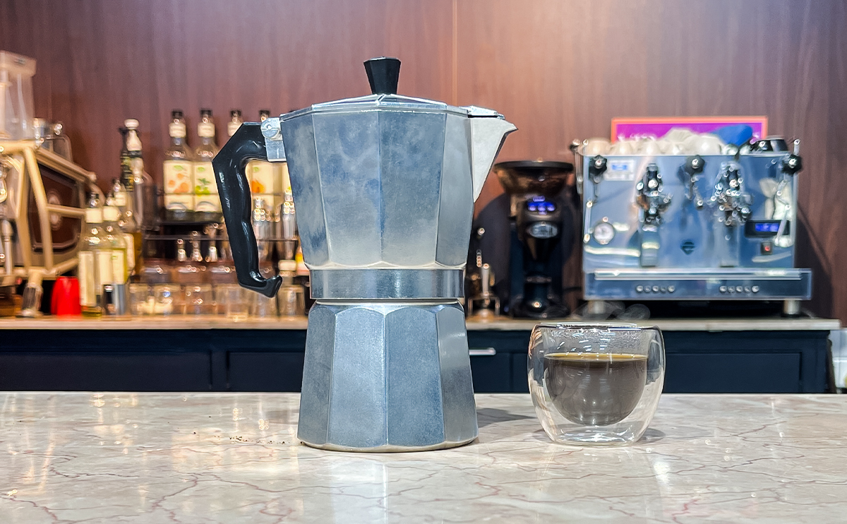 Moka pot on a stovetop with coffee rising into the top chamber