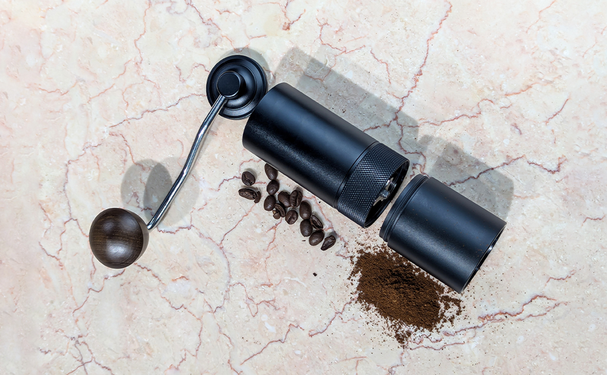 Hand coffee grinder held next to whole coffee beans